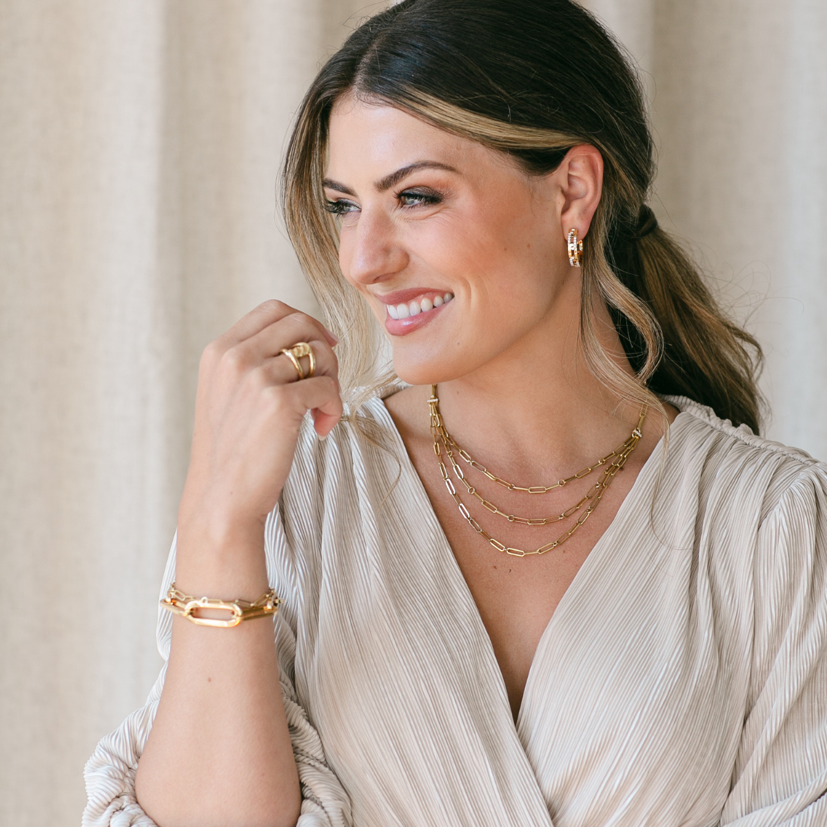 Woman wearing gold and rose gold jewelry while smiling out a window