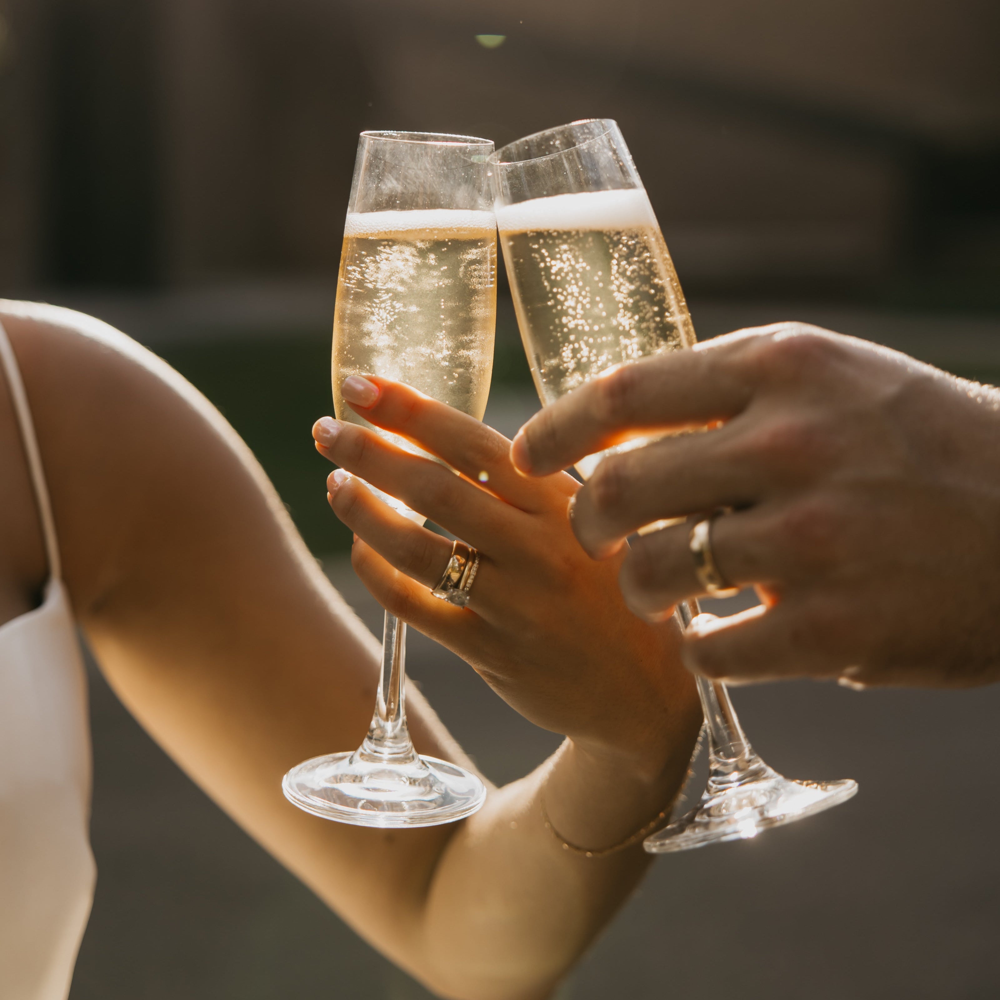 Champagne Flutes Clinking with Hands Wearing Engagement Ring & Wedding Bands