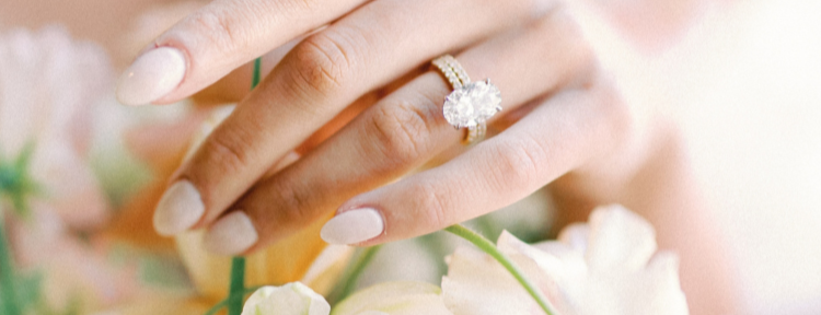 Hand wearing a gold ring with a diamond, holding flowers