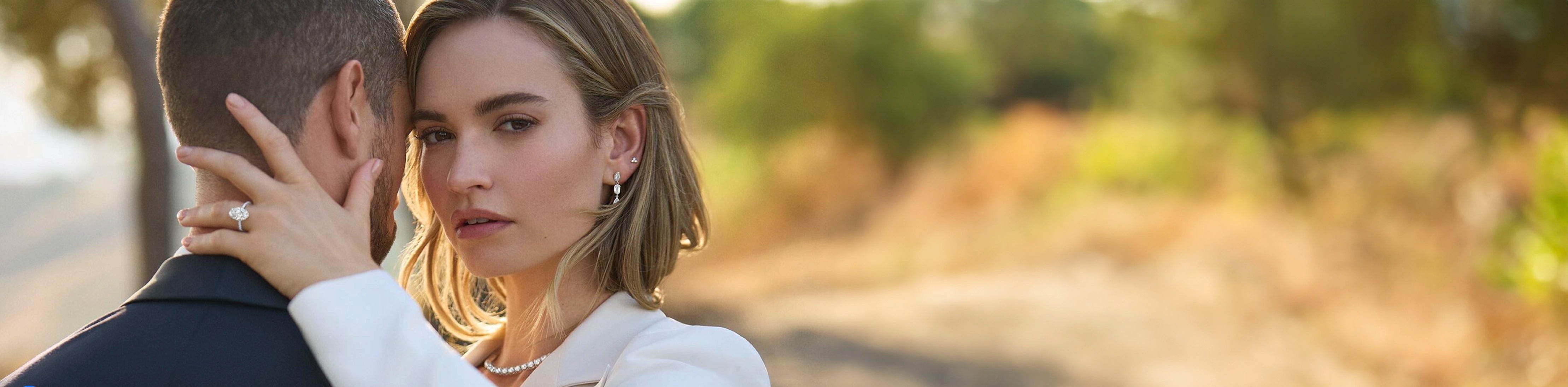 Man in a suit and a woman wearing jewelry embracing each other while outdoors