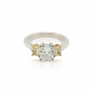 This three stone ring is crafted from platinum and 18k yellow gold and features a 1.51 carat radiant diamond and 0.69 total carats of fancy yellow radiant side diamonds.