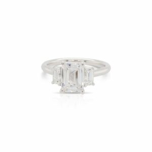 This diamond engagement ring mounting by Alyssa is crafted from 18k white gold and features 0.66 total carats of emerald cut side diamonds. The center diamond is chosen separately.