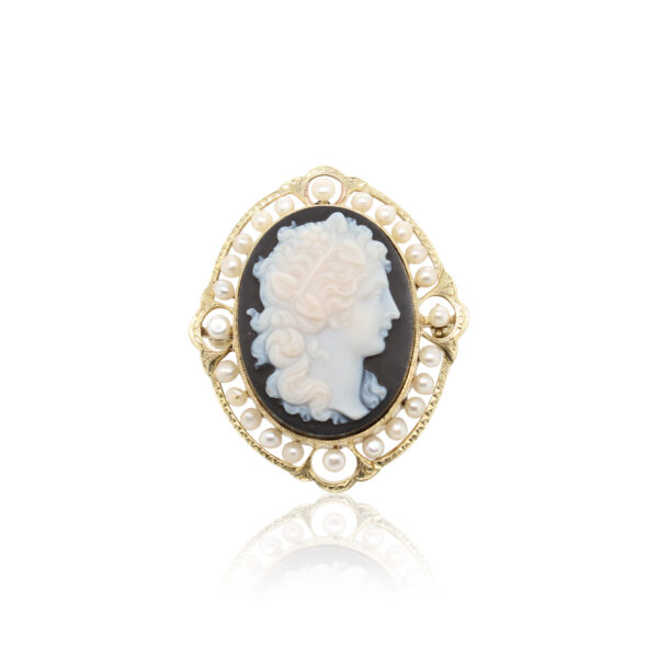 This brooch is crafted from 14k yellow gold and features a cameo with an onyx background and pearl edging.